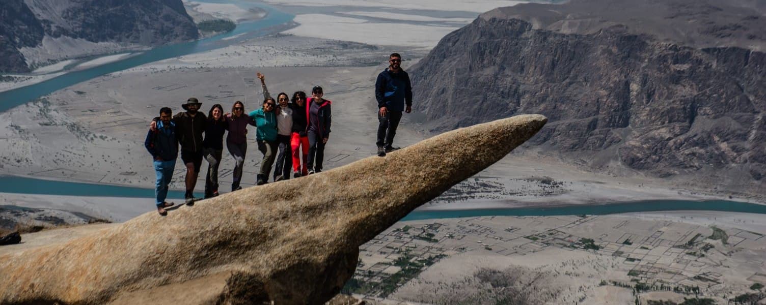 A small group of travellers standing on the tongue of Marsur Rock, high above the Indus and the Skardu valley in Gilgit-Baltistan